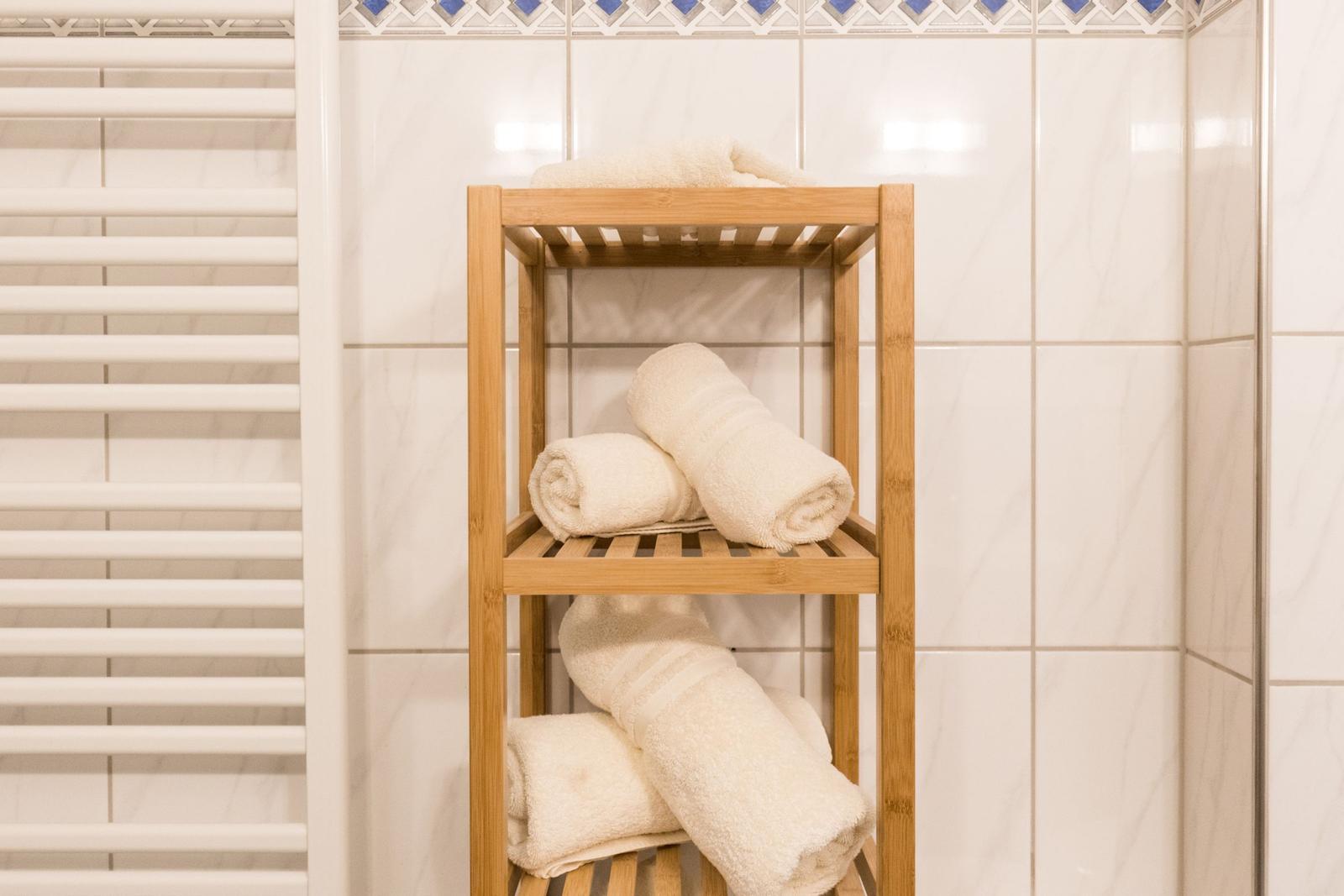 Holzregal mit Handtüchern in Badezimmer mit Fliesenwand und Heizung.