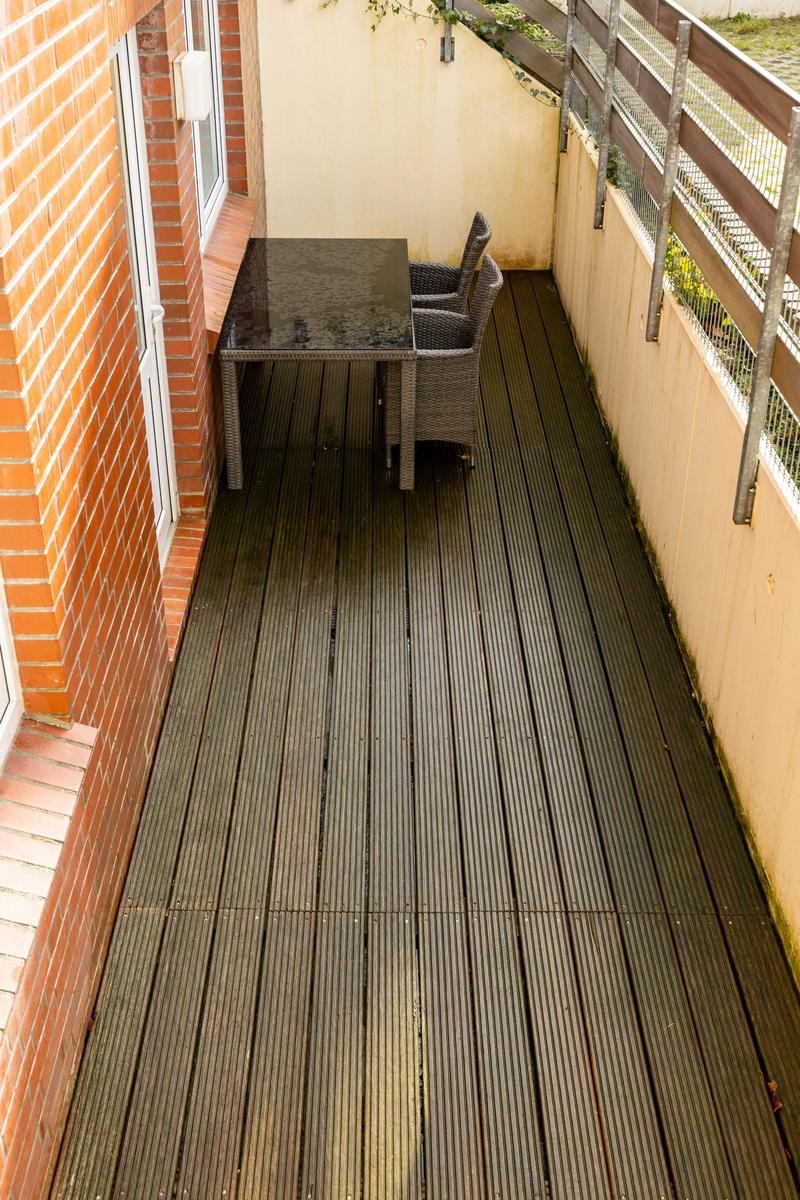 Terrasse mit Tisch und zwei Stühlen, Holzdielen und Brüstung.