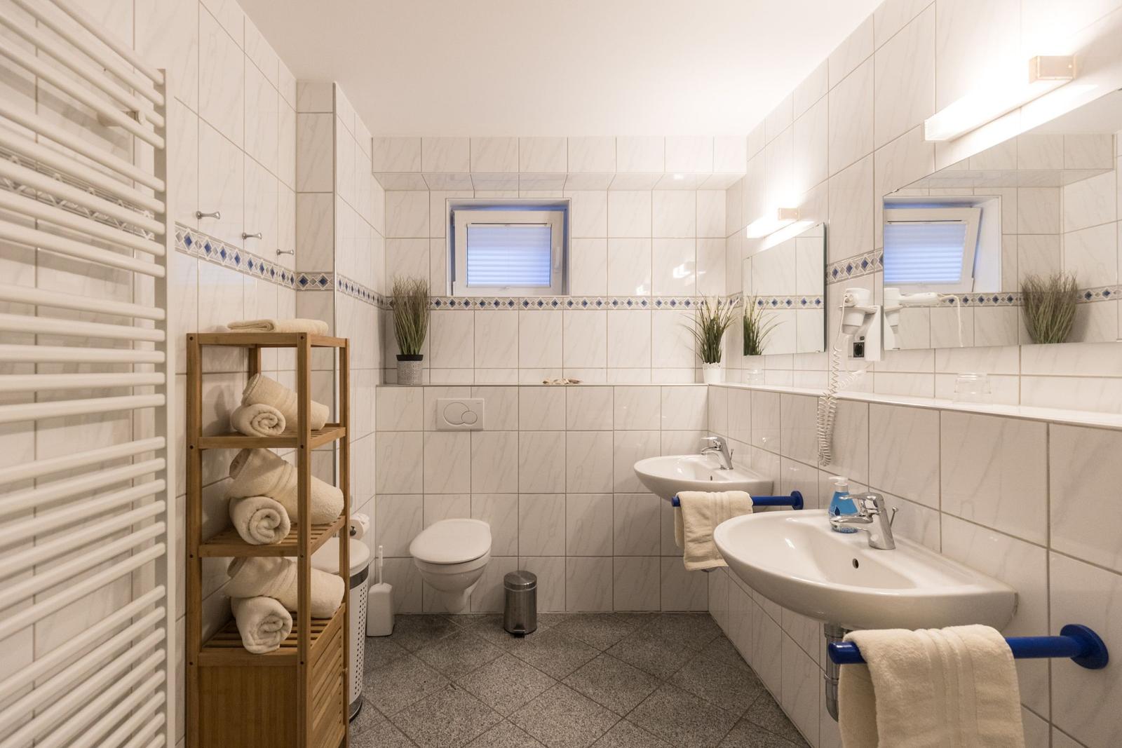 Badezimmer mit Dusche, Waschbecken und Toilette. Holzregal mit Handtüchern.