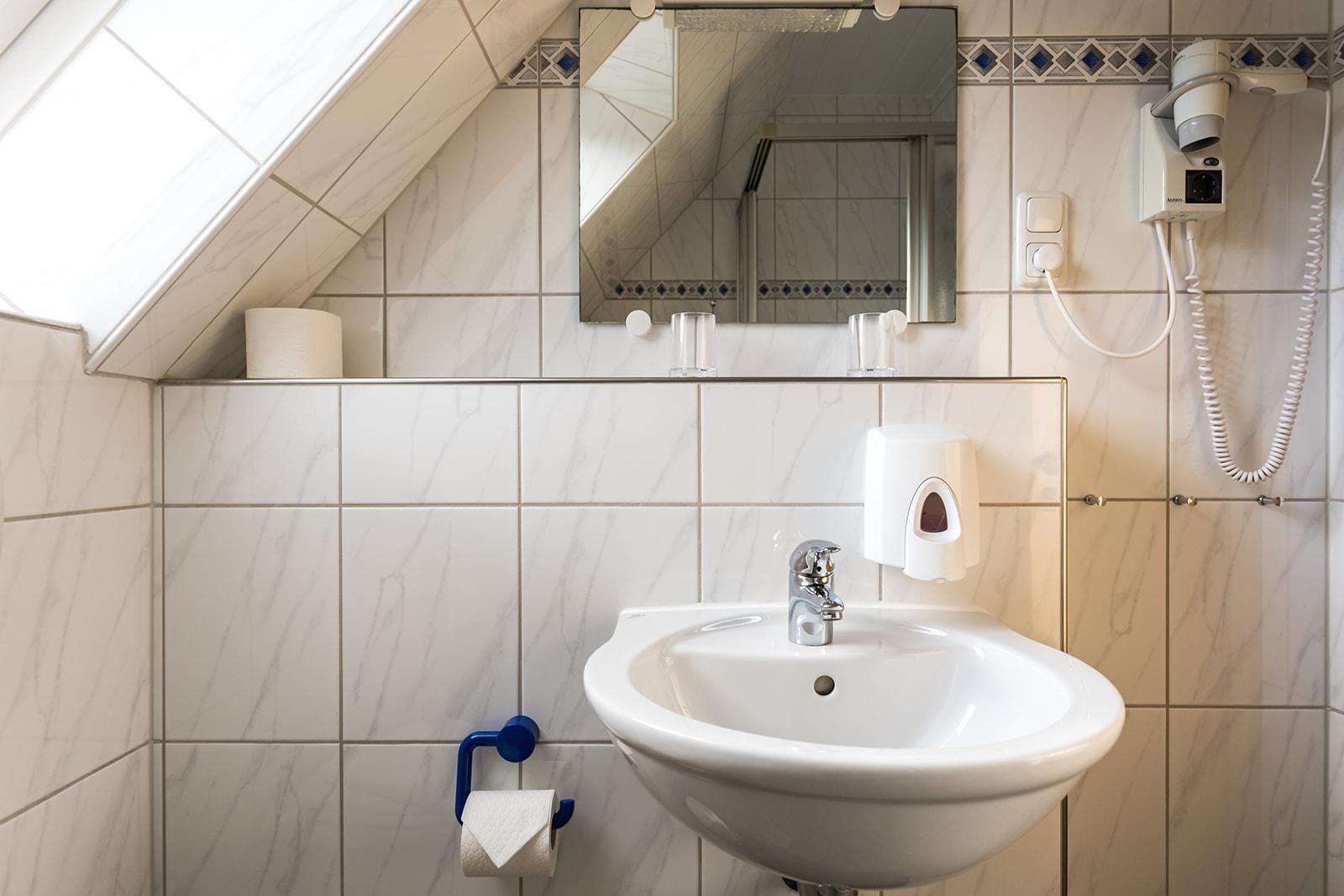 Badezimmer mit Waschbecken, Spiegel, Handtuchhalter und Haartrockner an der Wand.
