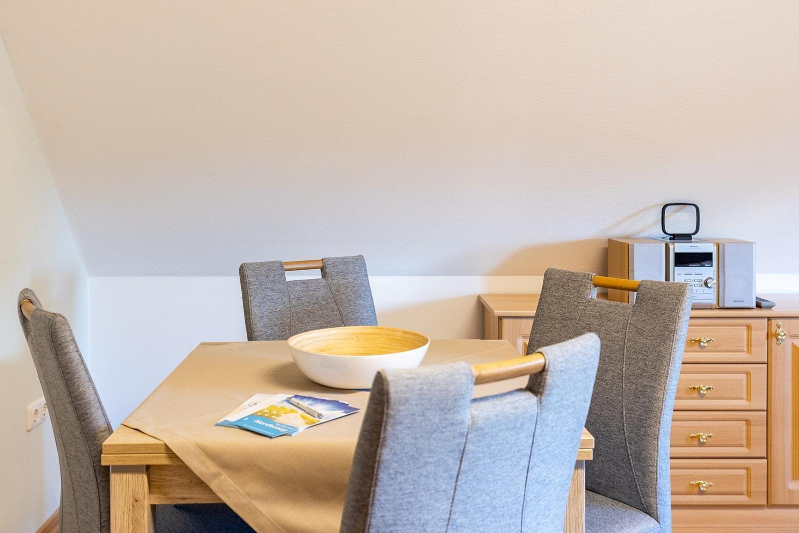 Esstisch mit vier Stühlen, Schrank und Radio in einem Raum mit geneigtem Dach.
