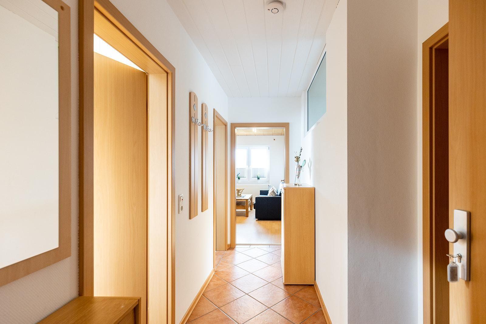 Flur mit Holztüren und Terrakottboden, Blick in Wohnzimmer mit Sofa und Fenster.