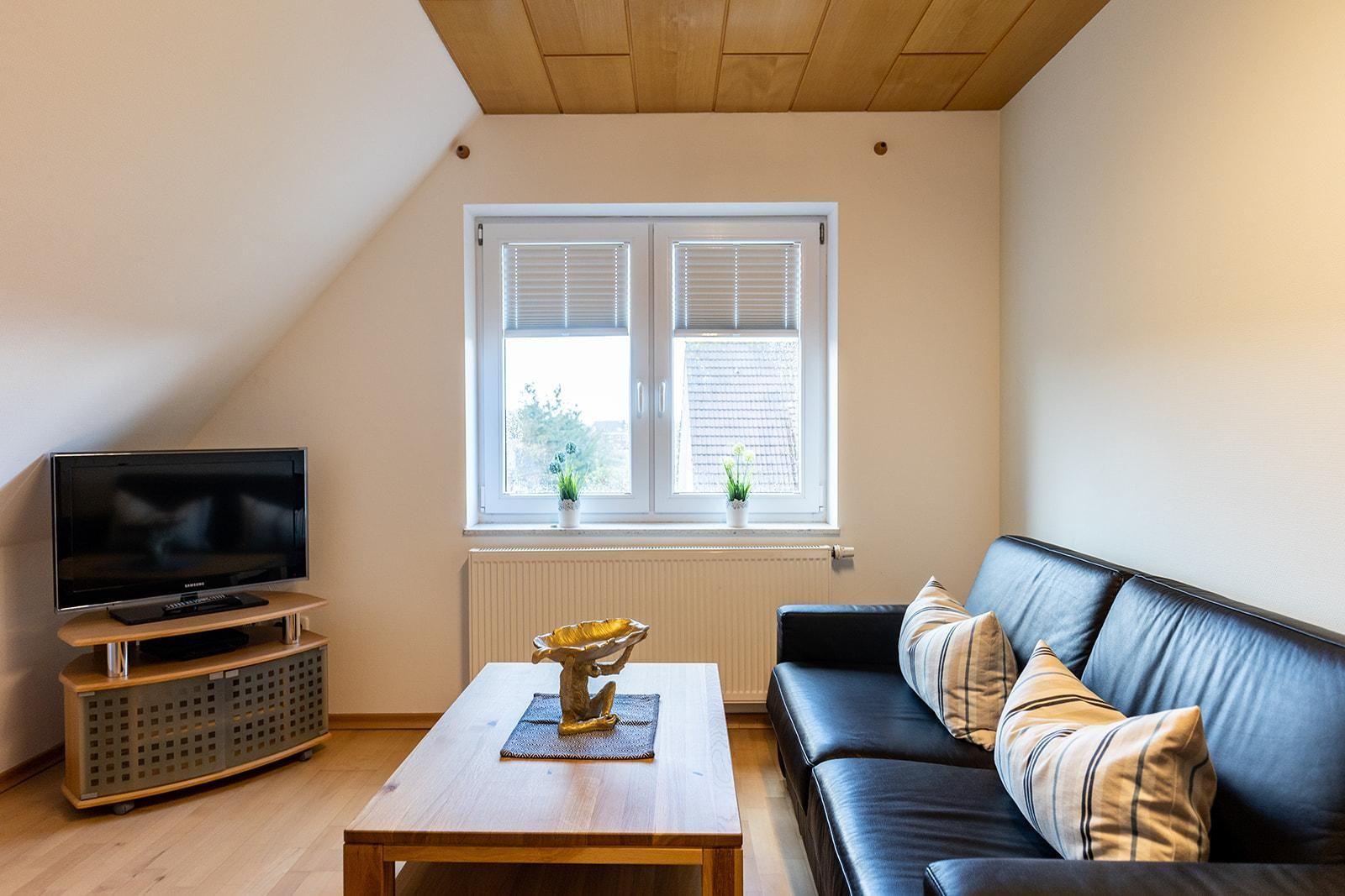 Wohnzimmer mit Sofa, Couchtisch und Fernseher unter Dachschrägen.