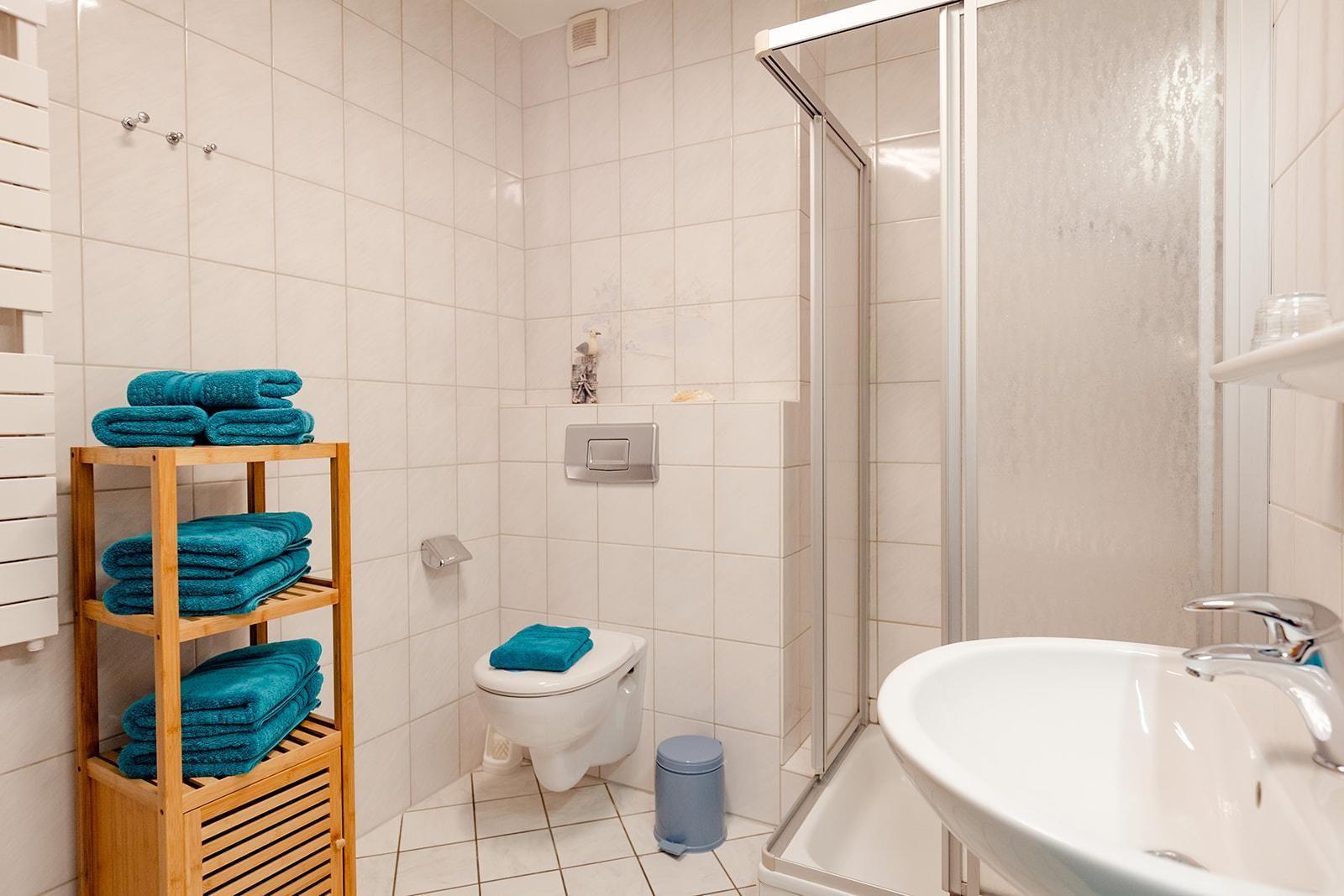 Badezimmer mit Dusche, Toilette und Waschbecken. Holzregal mit blauen Handtüchern.