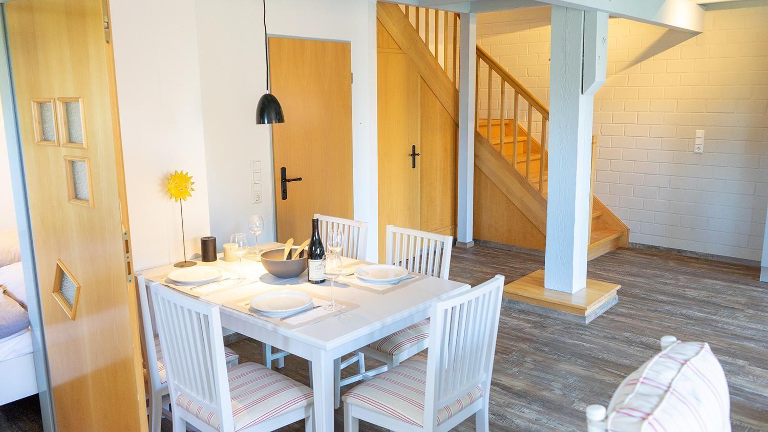 Esstisch mit vier Stühlen, Flur mit Holztreppe und weiße Wände.