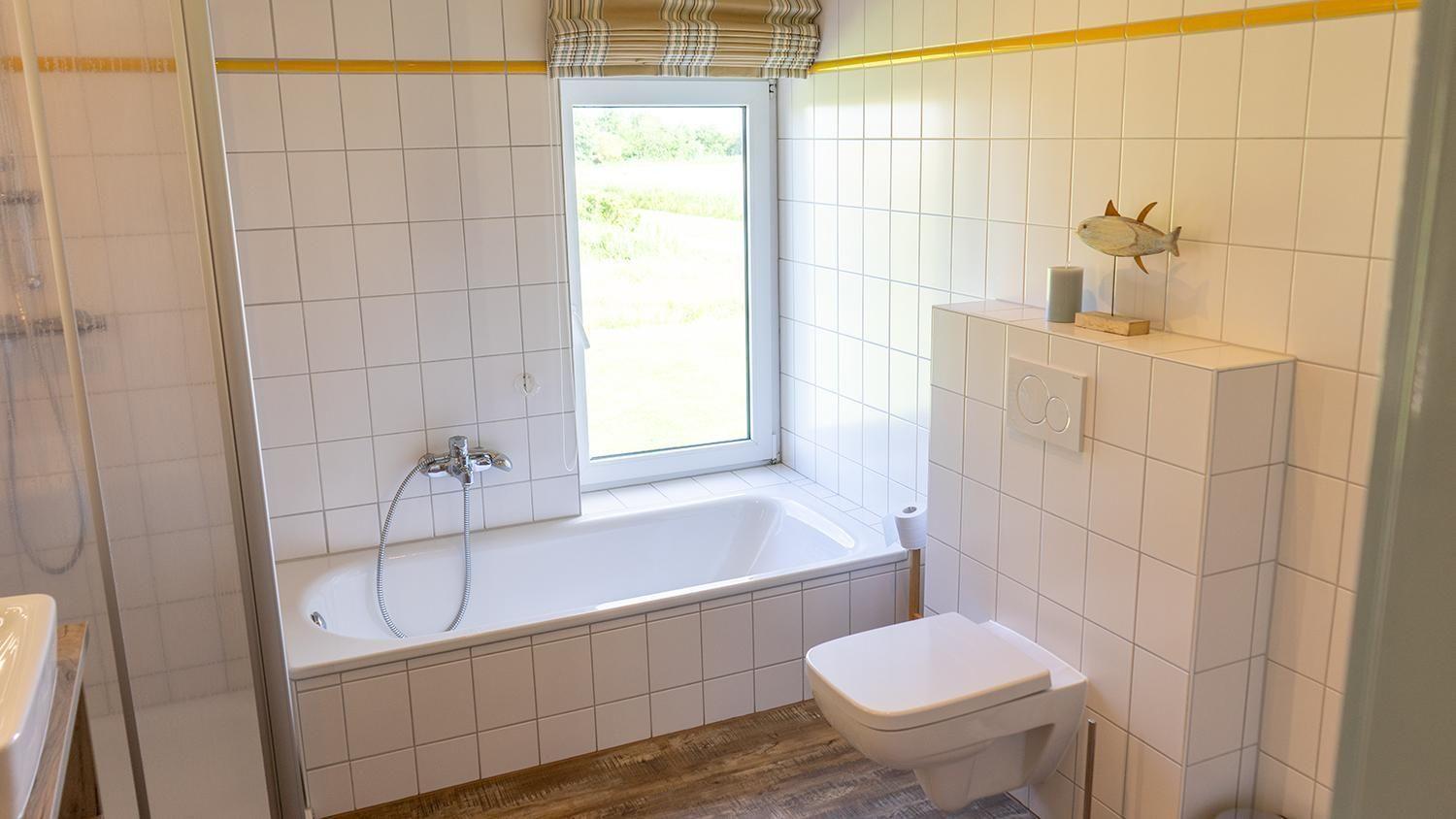 Badezimmer mit Badewanne, Fenster und Toilette. Wandfliesen und Holzboden.
