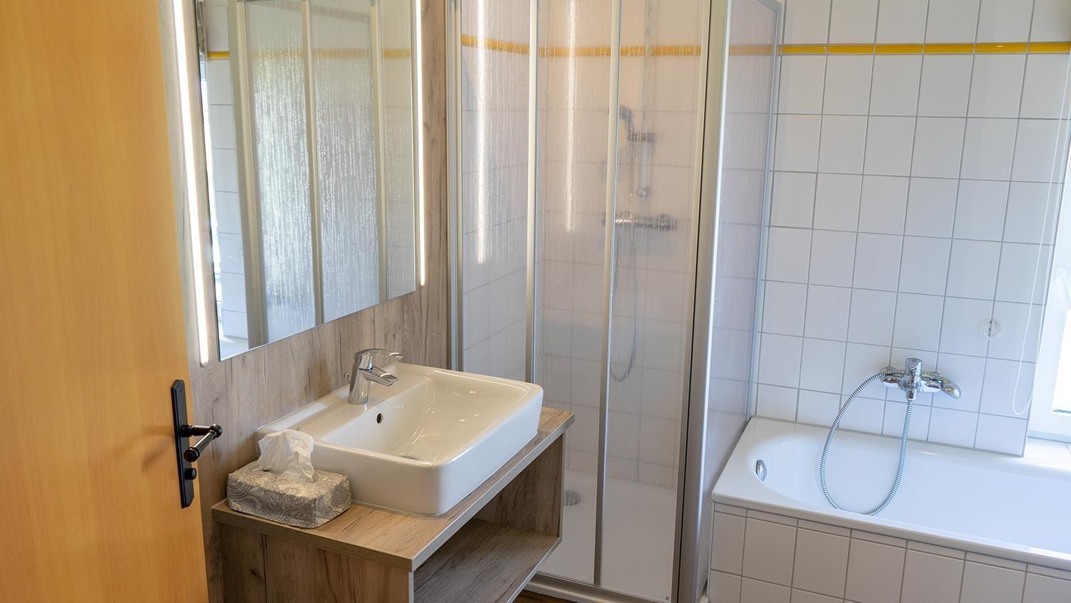 Badezimmer mit Dusche, Badewanne und Waschbecken mit Spiegel.