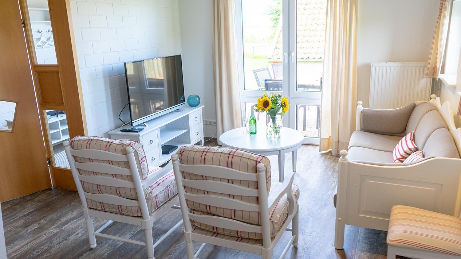 Wohnzimmer mit Sofa, zwei Stühlen, TV und Tisch mit Sonnenblumen.