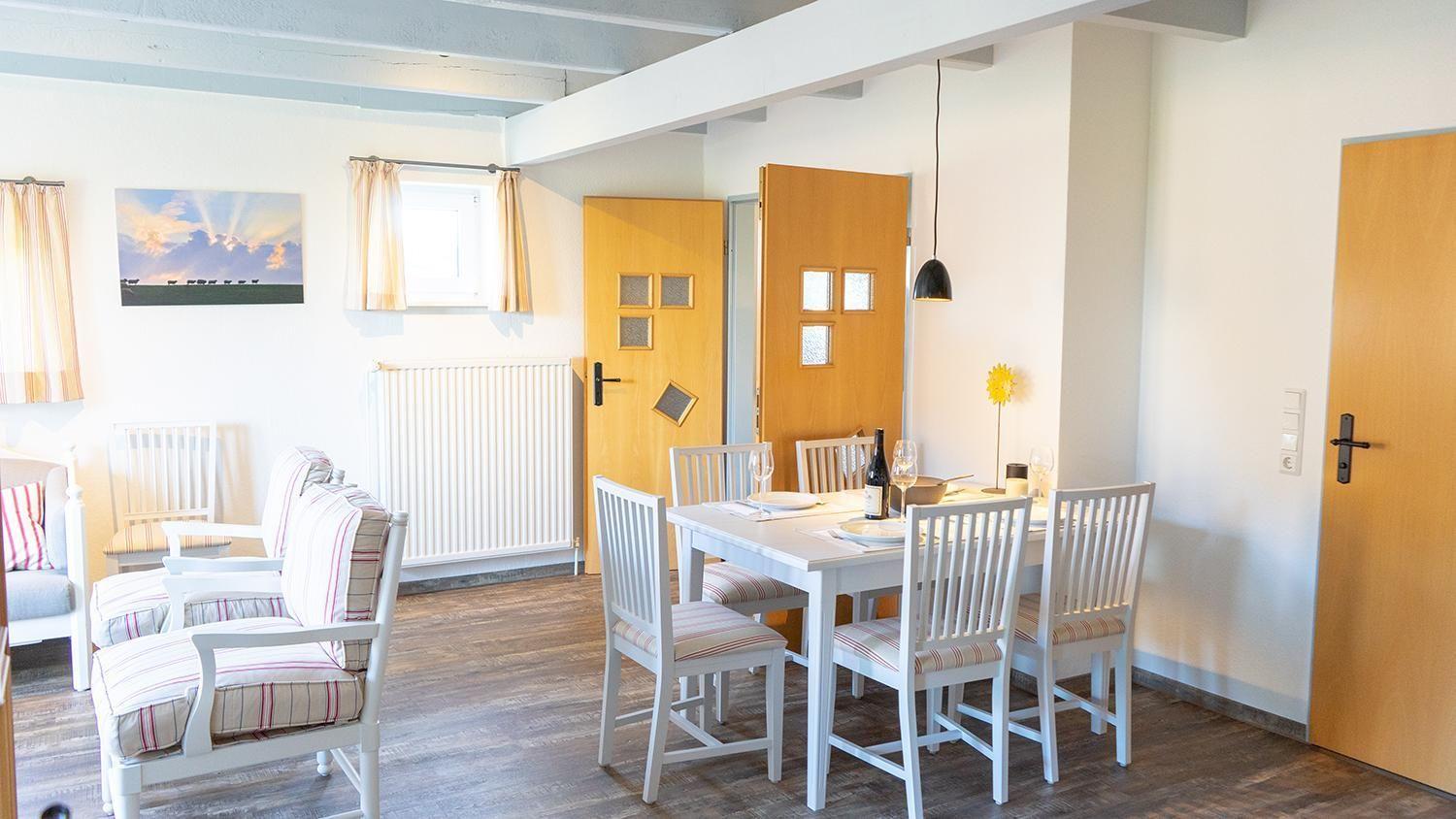 Wohn- und Essbereich mit Tisch, Stühlen und Sofa. Holzfußboden und weiße Wände.
