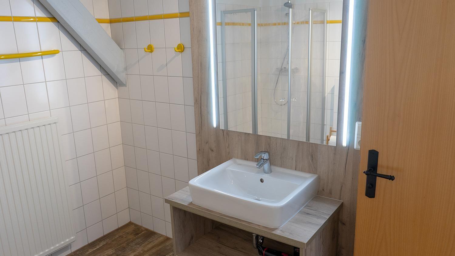 Bathroom with sink, mirror, and shower. Wall cladding and floor are wood.