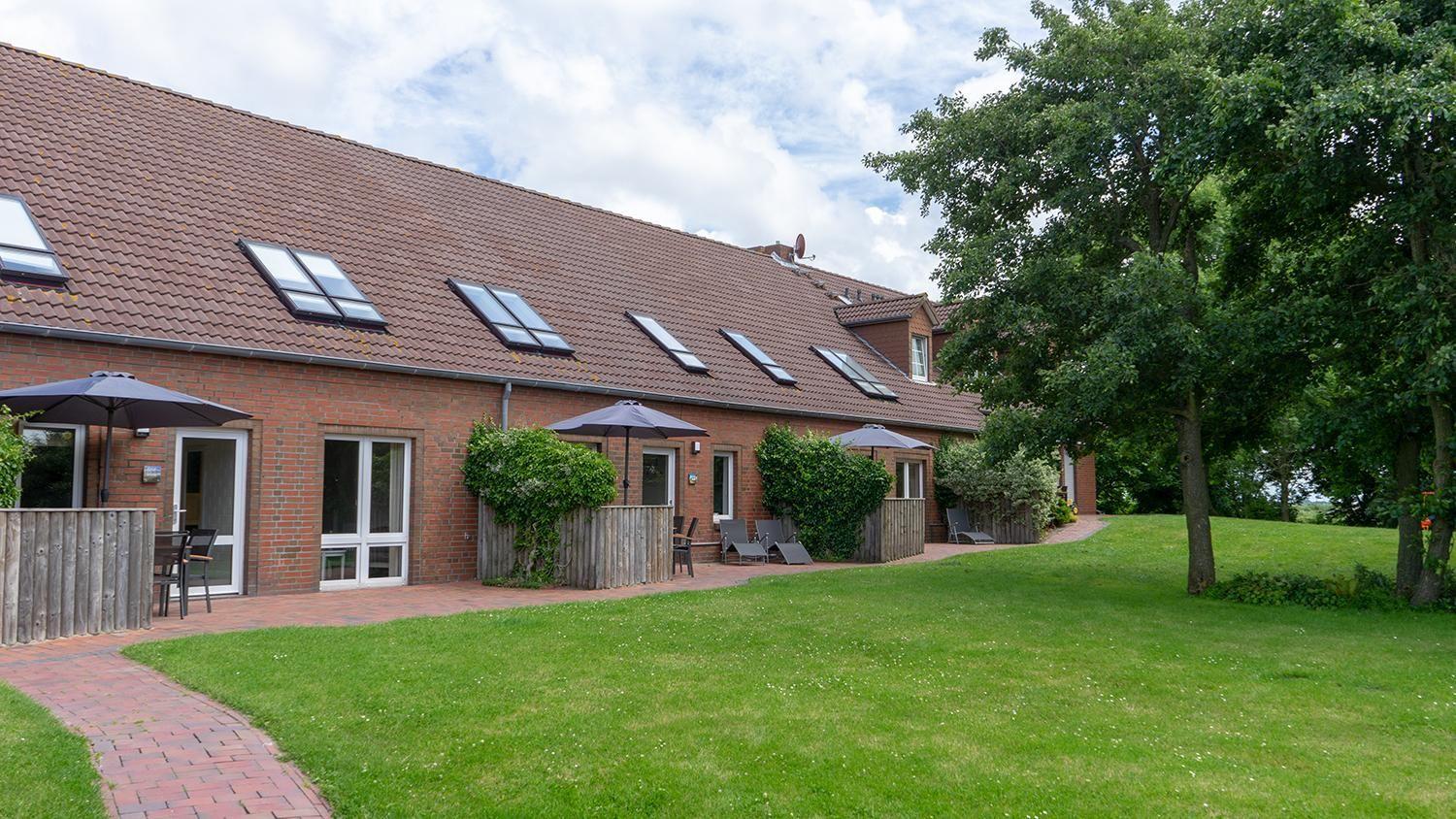 Red brick house with skylights, terrace with umbrellas, and green lawn.