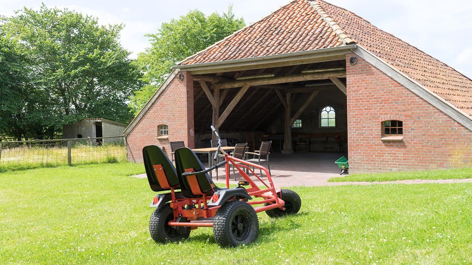 Red go-kart on green lawn in front of brick barn with wooden beams.