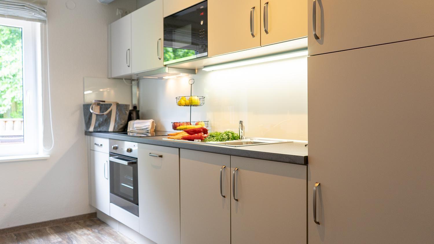 Kitchen with white cabinets, stove, sink, and window with view outside.