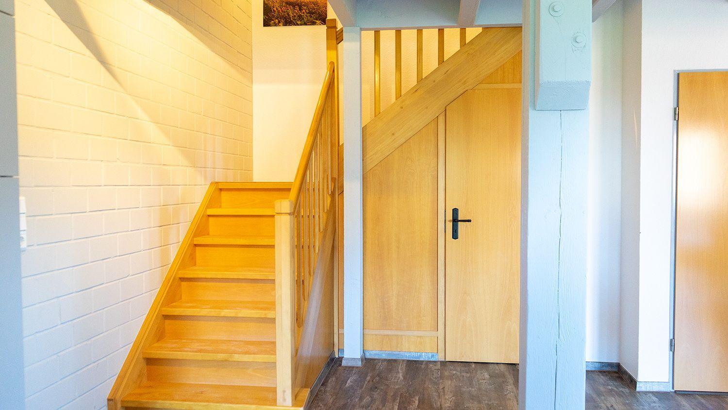 Wooden staircase with handrail leads to upper level. Wooden door with black handle.