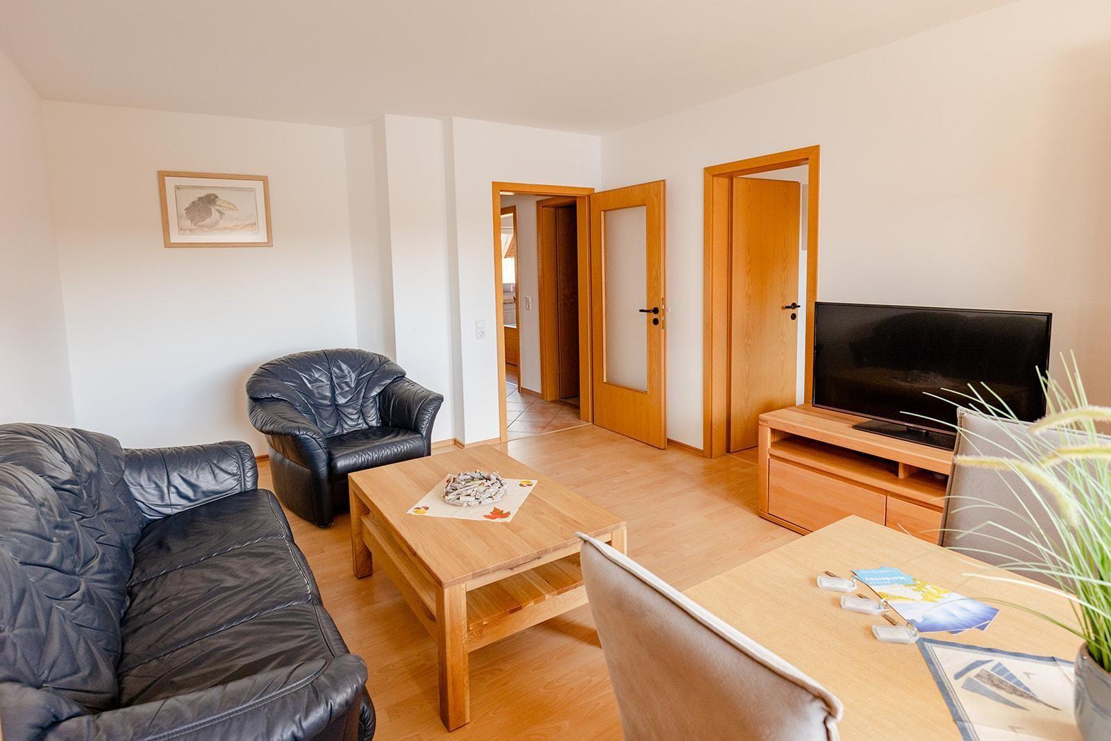 Wohnzimmer mit Sofa, Sessel, Couchtisch und Fernseher.