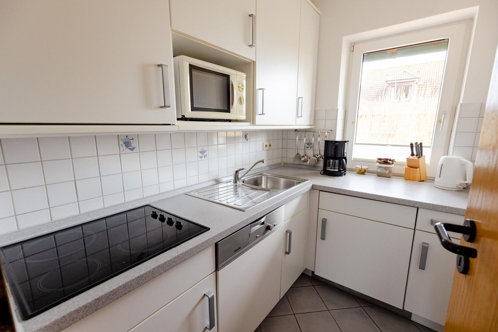 Küche mit weißen Schränken, Herd, Spüle und Fenster.