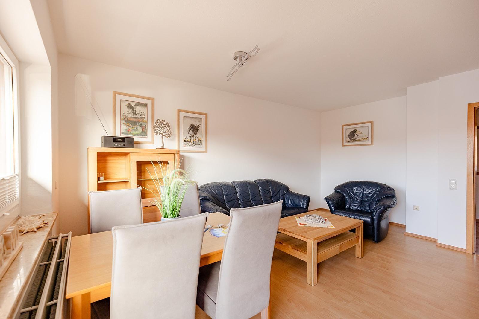 Wohn- und Essbereich mit Sofa, Sessel, Tisch und Stühlen sowie Wandbildern.