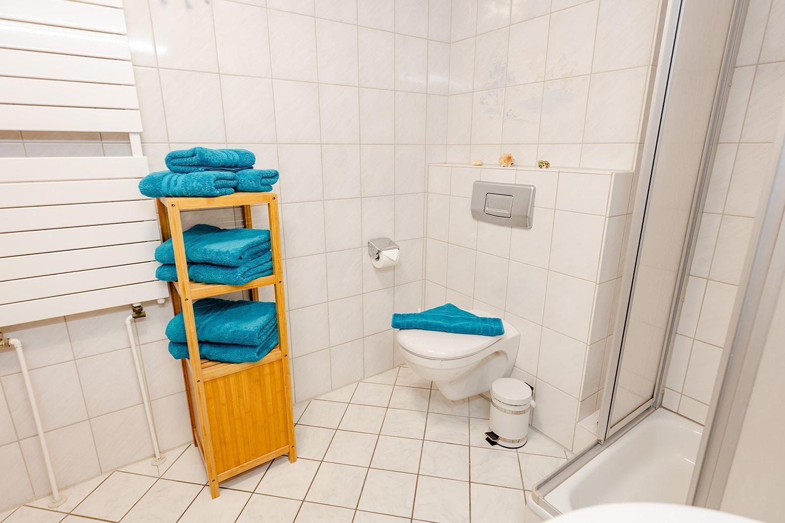 Badezimmer mit Toilette, Dusche und Holzregal mit blauen Handtüchern.