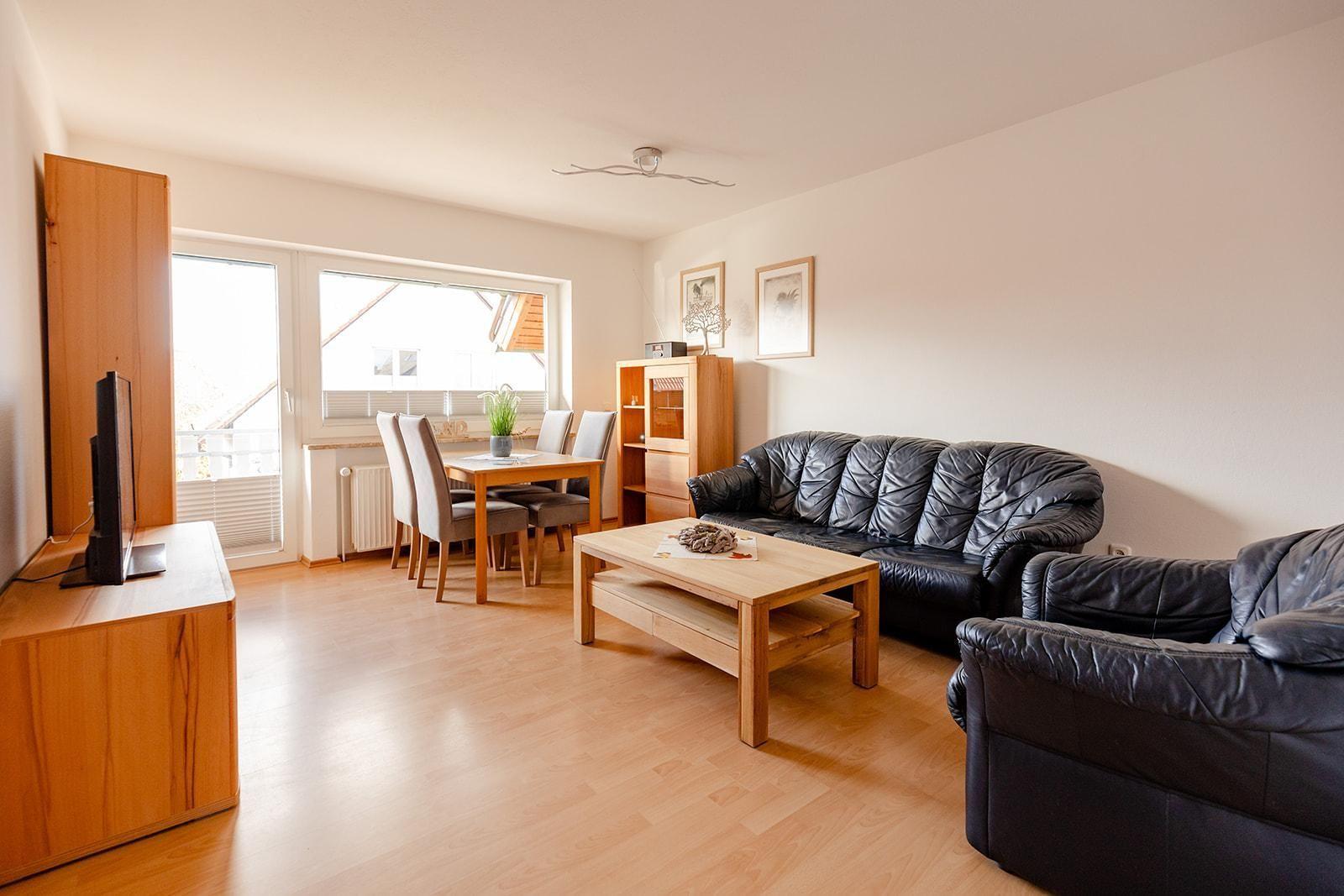 Wohn- und Essbereich mit Holzmöbeln, Ledersofa und TV. Durchgang zum Balkon.
