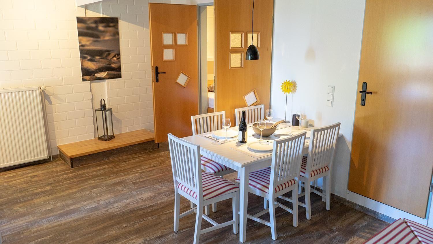 Essbereich mit weißem Tisch und Stühlen, Holzboden und Tür zu Schlafzimmer.
