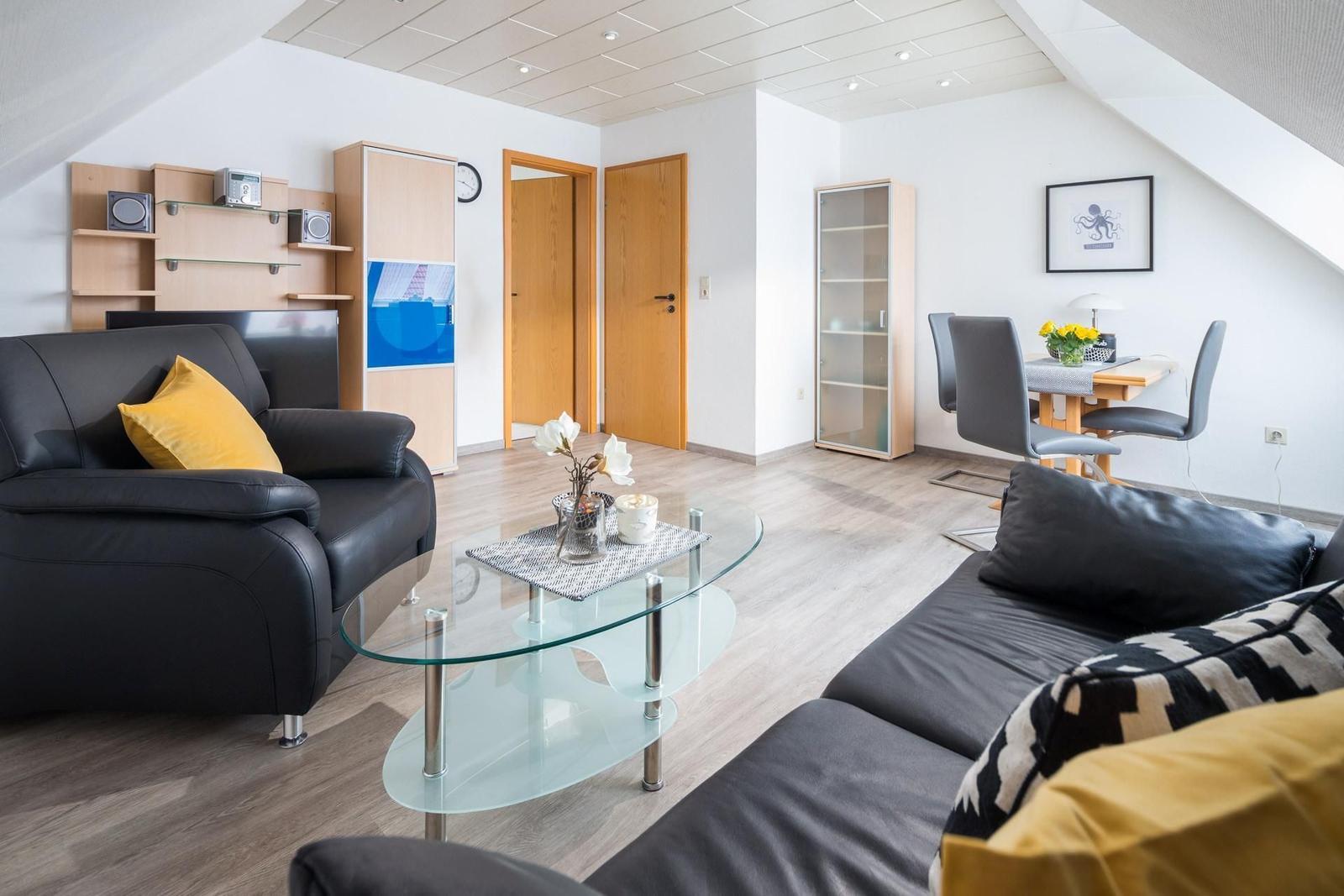 Wohnzimmer mit Sofa, Couchtisch und Essbereich unter Dachschräge