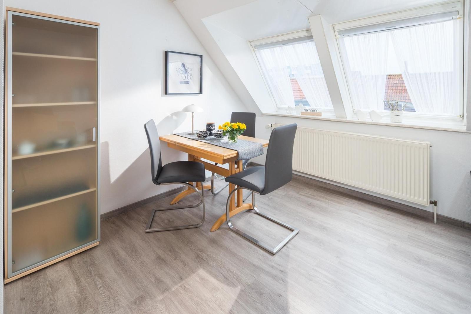 Essbereich mit Tisch, Stühlen und Schrank unter Dachschrägen mit Fenstern.