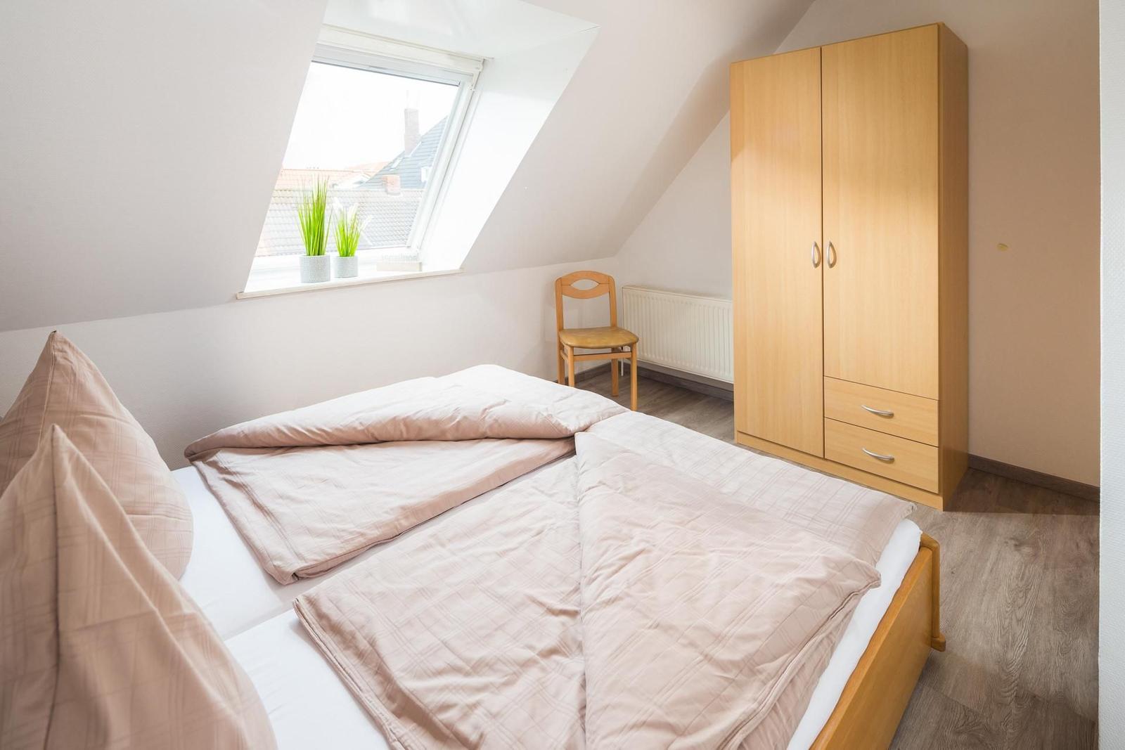 Schlafzimmer mit Dachfenster, Bett, Kleiderschrank und Stuhl.