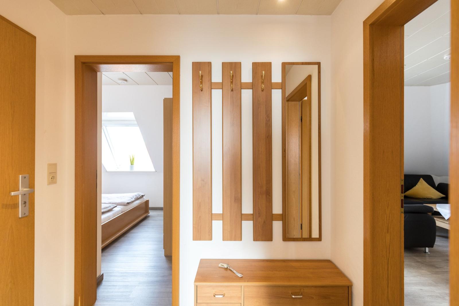 Eingangsbereich mit Holzgarderobe, Spiegel und Schreibtisch. Links Schlafzimmer, rechts Wohnzimmer.