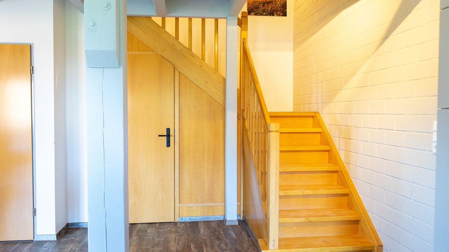 Holztreppe mit Geländer führt zu einer Tür. Weiße Ziegelwand und Holzboden.