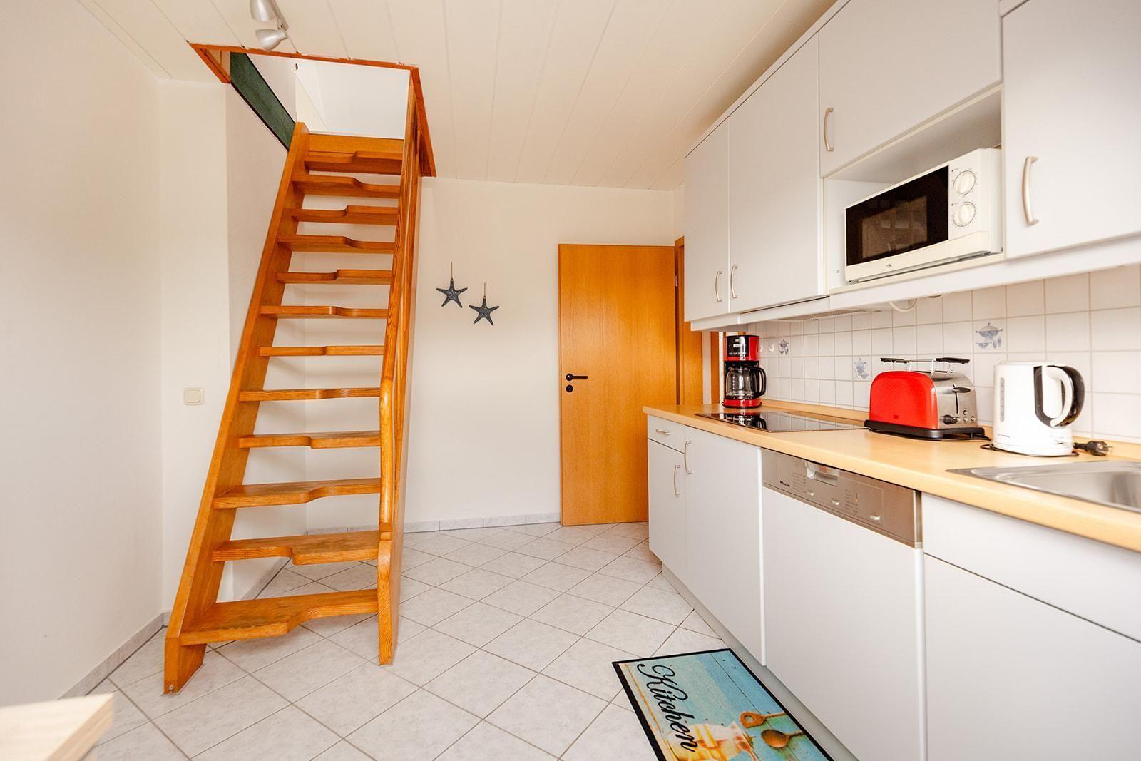 Küche mit weißen Schränken, rotem Toaster und Holztreppe zur oberen Etage.