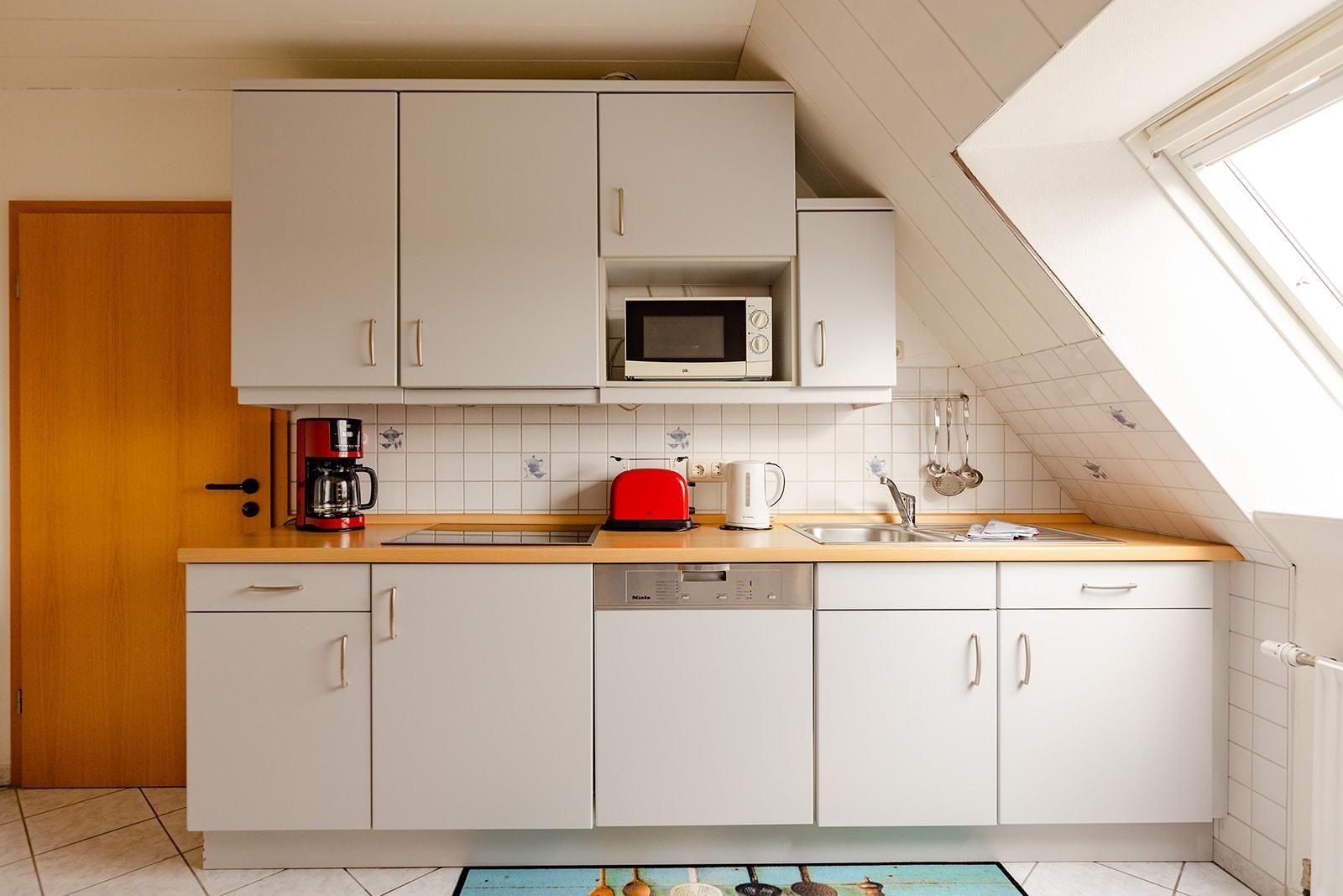 Küche mit weißen Schränken, rotem Toaster und Mikrowelle unter Dachschräge.