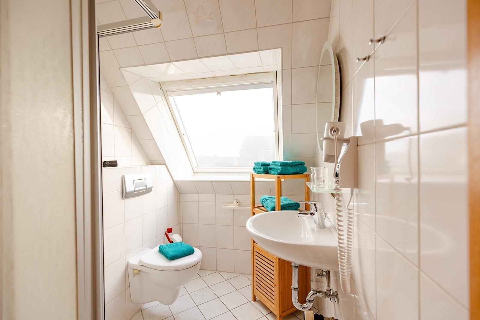 Badezimmer mit Toilette, Waschbecken und Dachfenster. Türkis Handtücher und Holzregal.