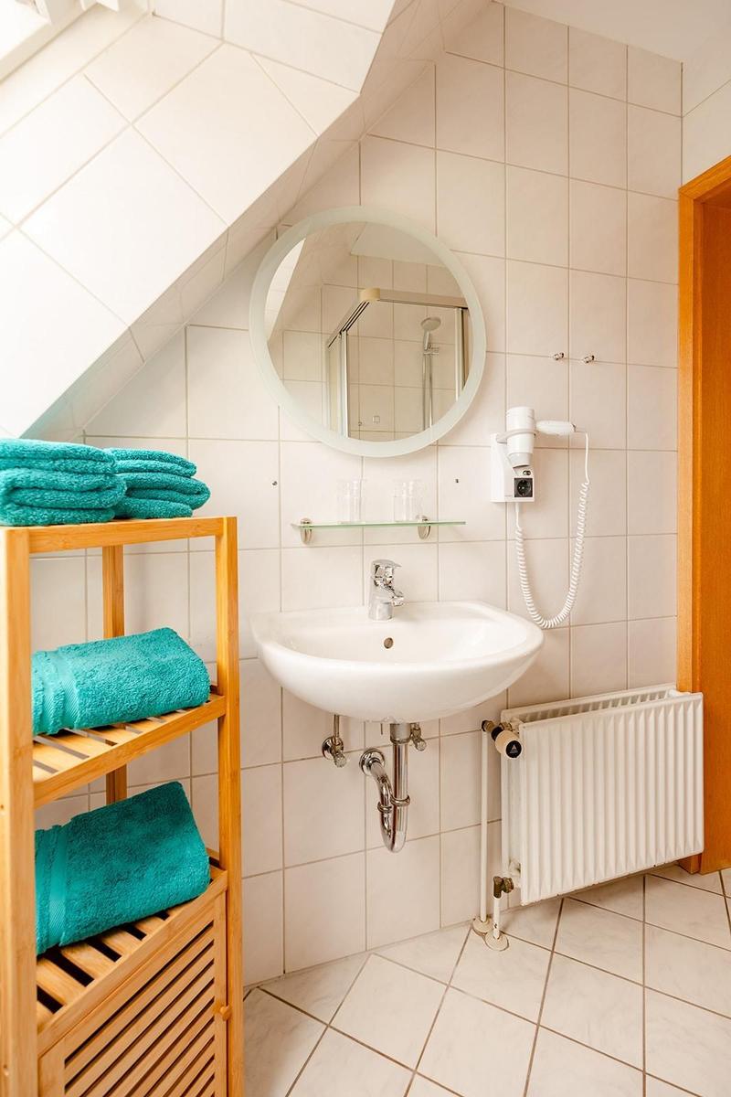 Badezimmer mit Waschbecken, Spiegel, Handtuchhalter und Heizkörper.