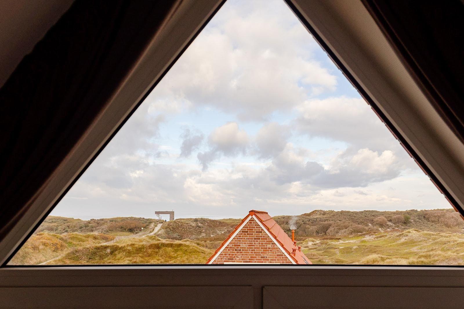 Dachfensterblick auf Dünenschilf und roten Ziegeldach