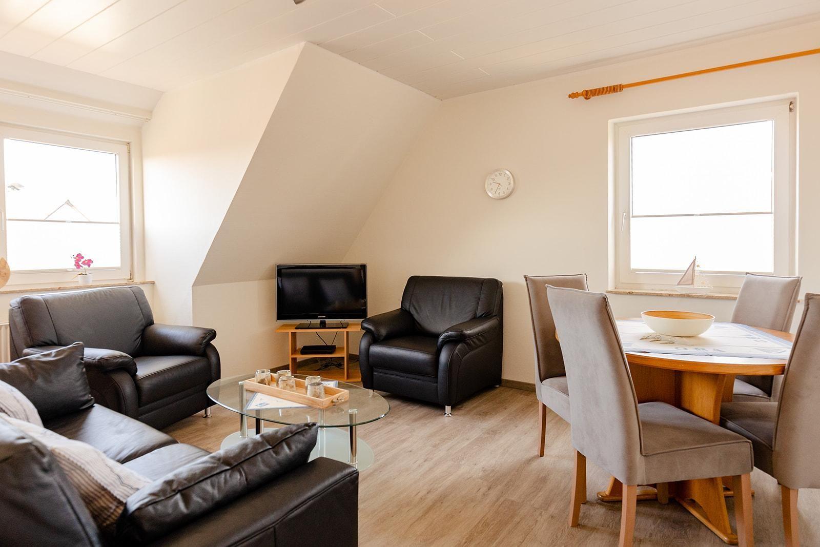 Wohn- und Essbereich mit Ledersofa, Fernseher und Holztisch.