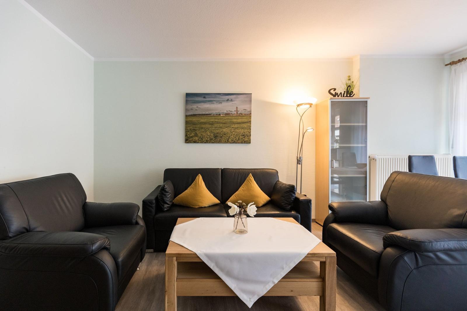 Wohnzimmer mit schwarzen Ledersofas, Holztisch und Wandbild.