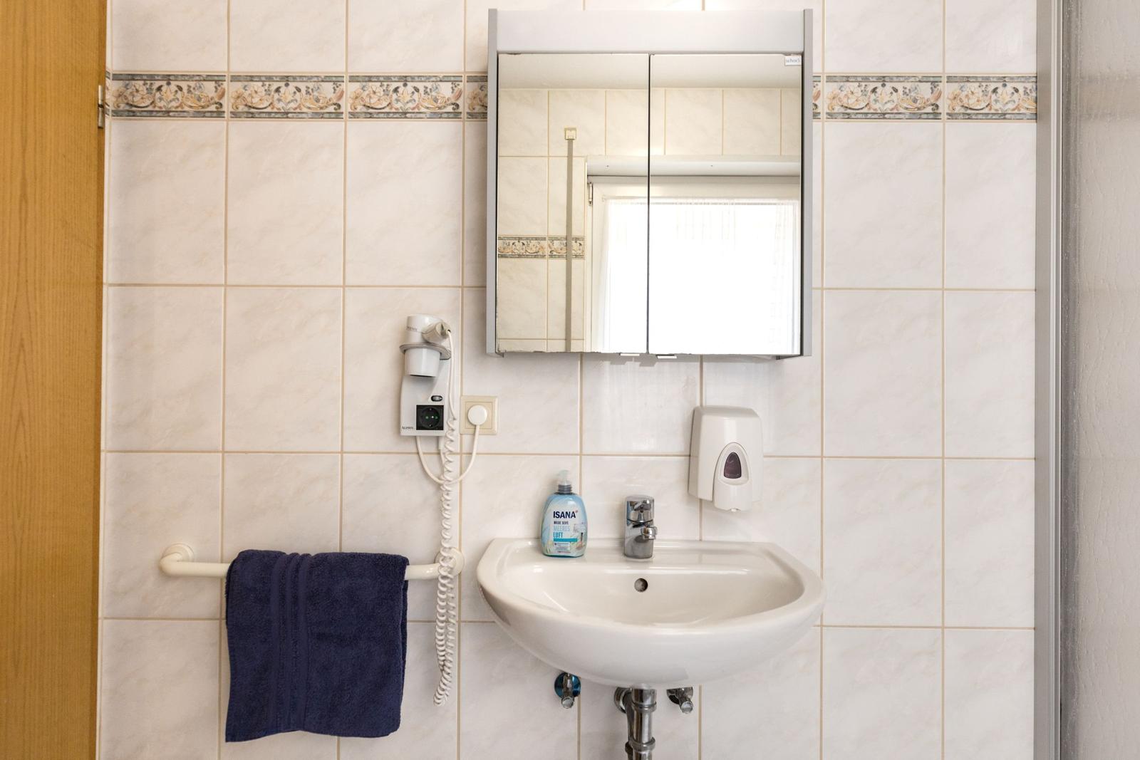 Badezimmer mit Waschbecken, Spiegel, Handtuch und Haartrockner an der Wand.