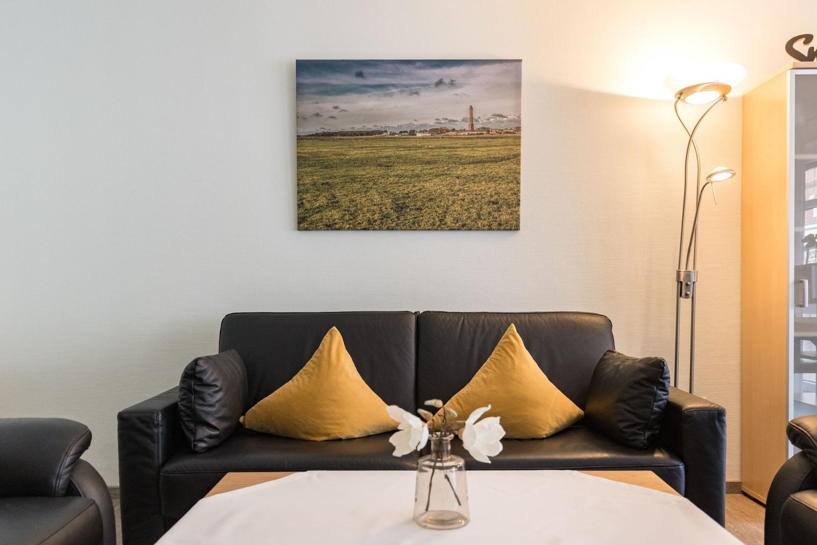 Schwarzes Sofa mit gelben Kissen, Wandbild und Stehlampe im Wohnzimmer.