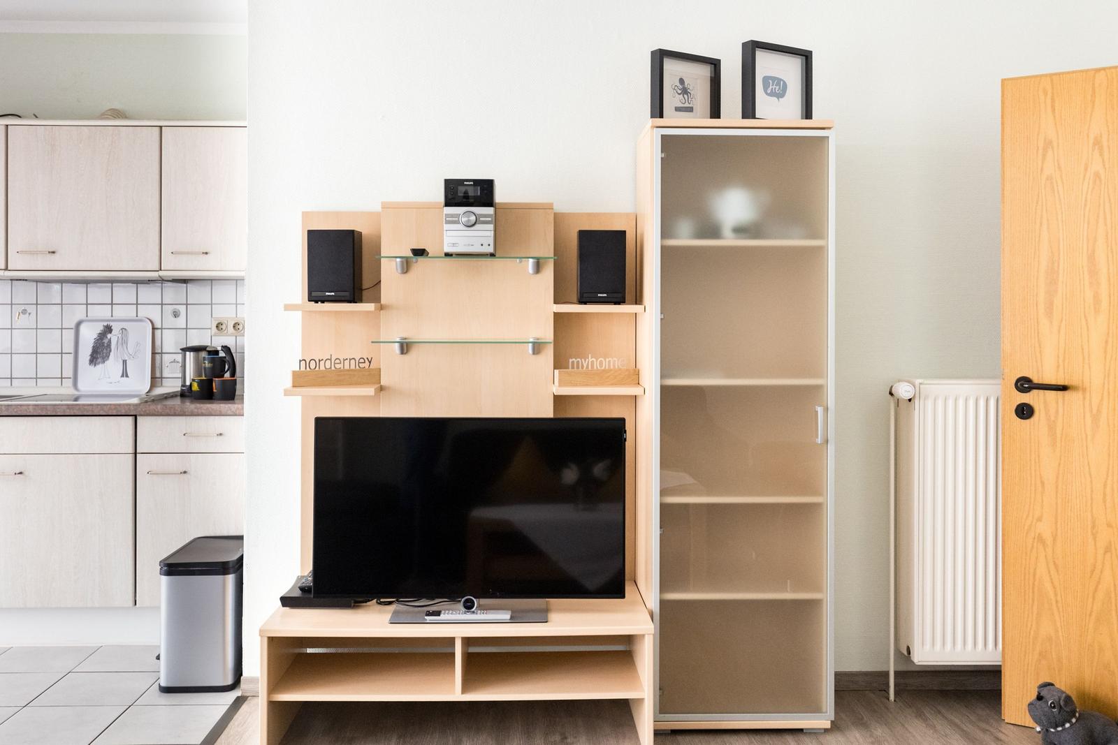 TV-Möbel mit Lautsprechern und Glasböden, daneben hängende Bilder und ein Schrank mit Glasfront.