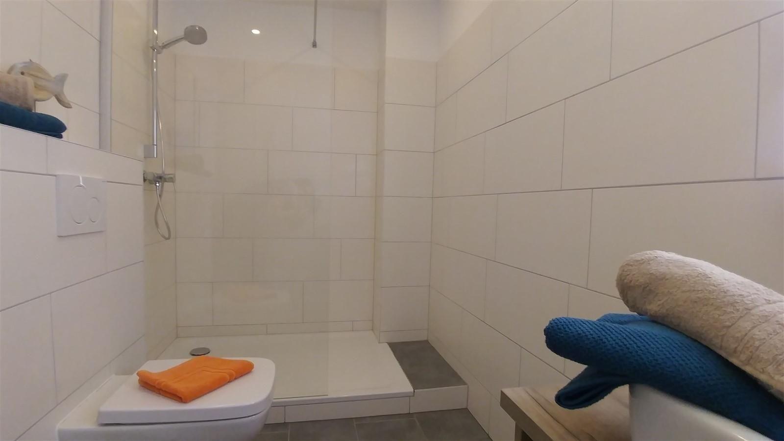 Dusche mit Duschbrause, Toilette und Handtücher auf Bänken