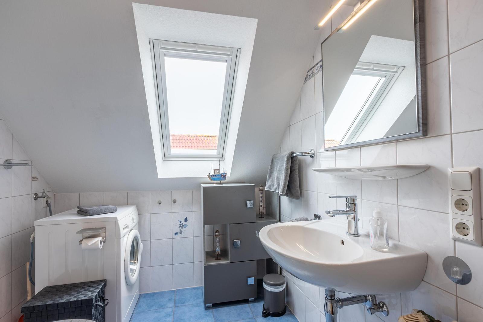 Badezimmer mit Waschmaschine, Spiegel und Dachfenster. Fliesen und blaue Bodenfliesen.