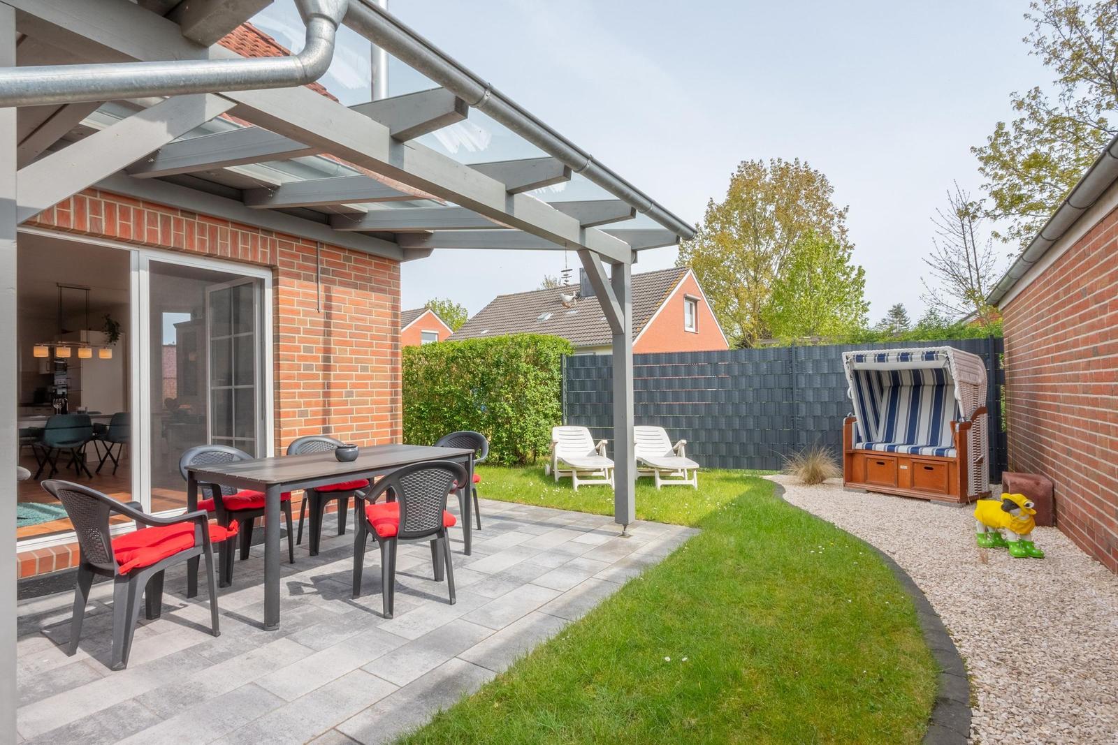 Terrasse mit Tisch, Stühlen und Sonnenschutz. Garten mit Liegen und Strandkorb.