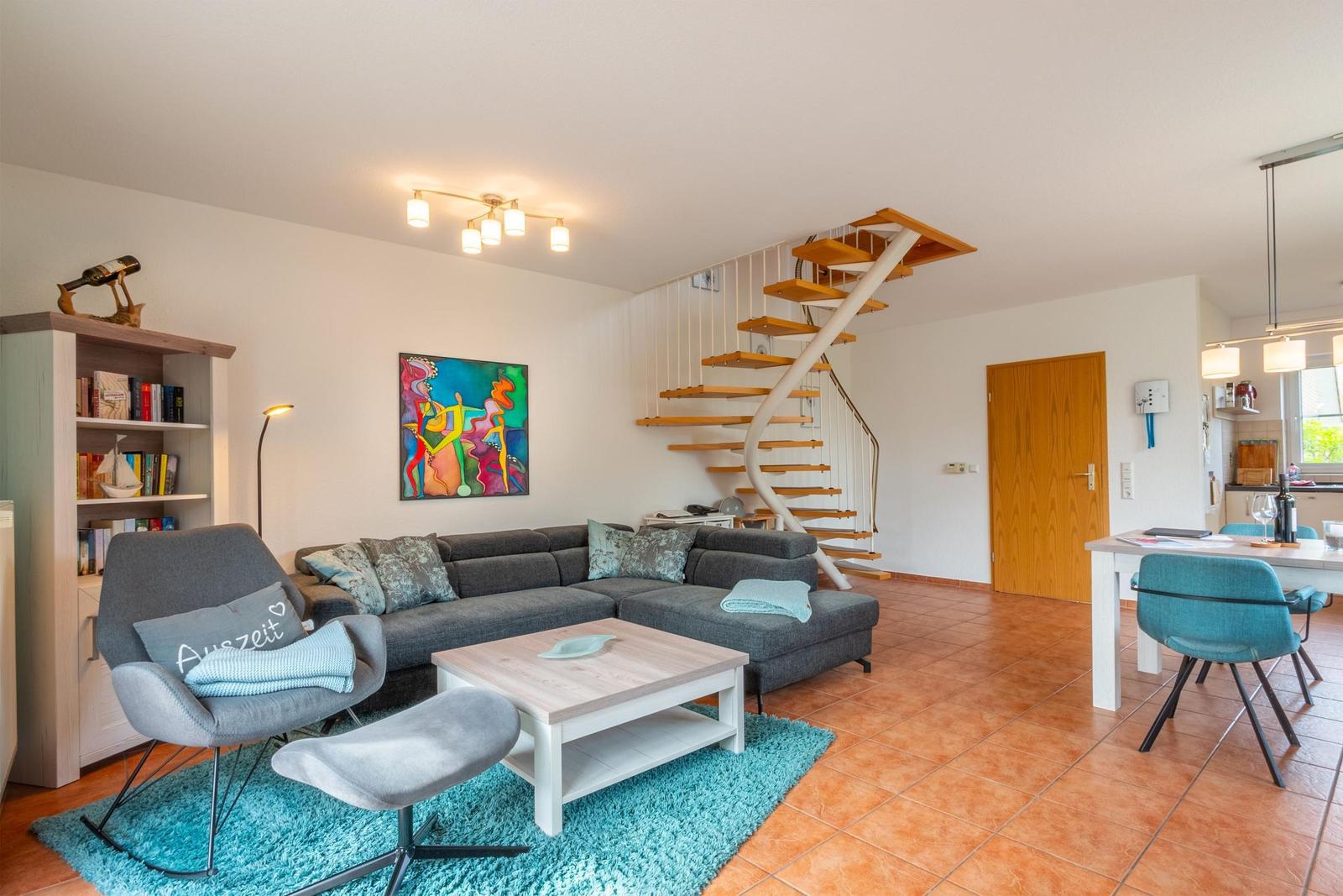 Wohnbereich mit Sofa, Sessel und Treppe zur oberen Etage.