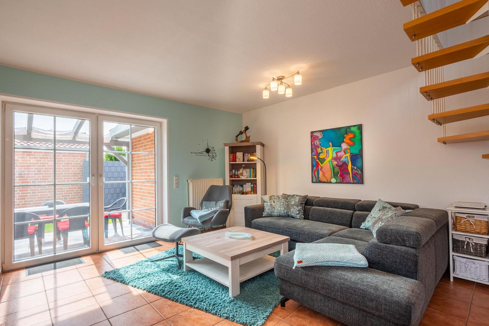 Wohnzimmer mit Sofa, Couchtisch und Terrassentür. Holztreppe und Wandbild sind sichtbar.