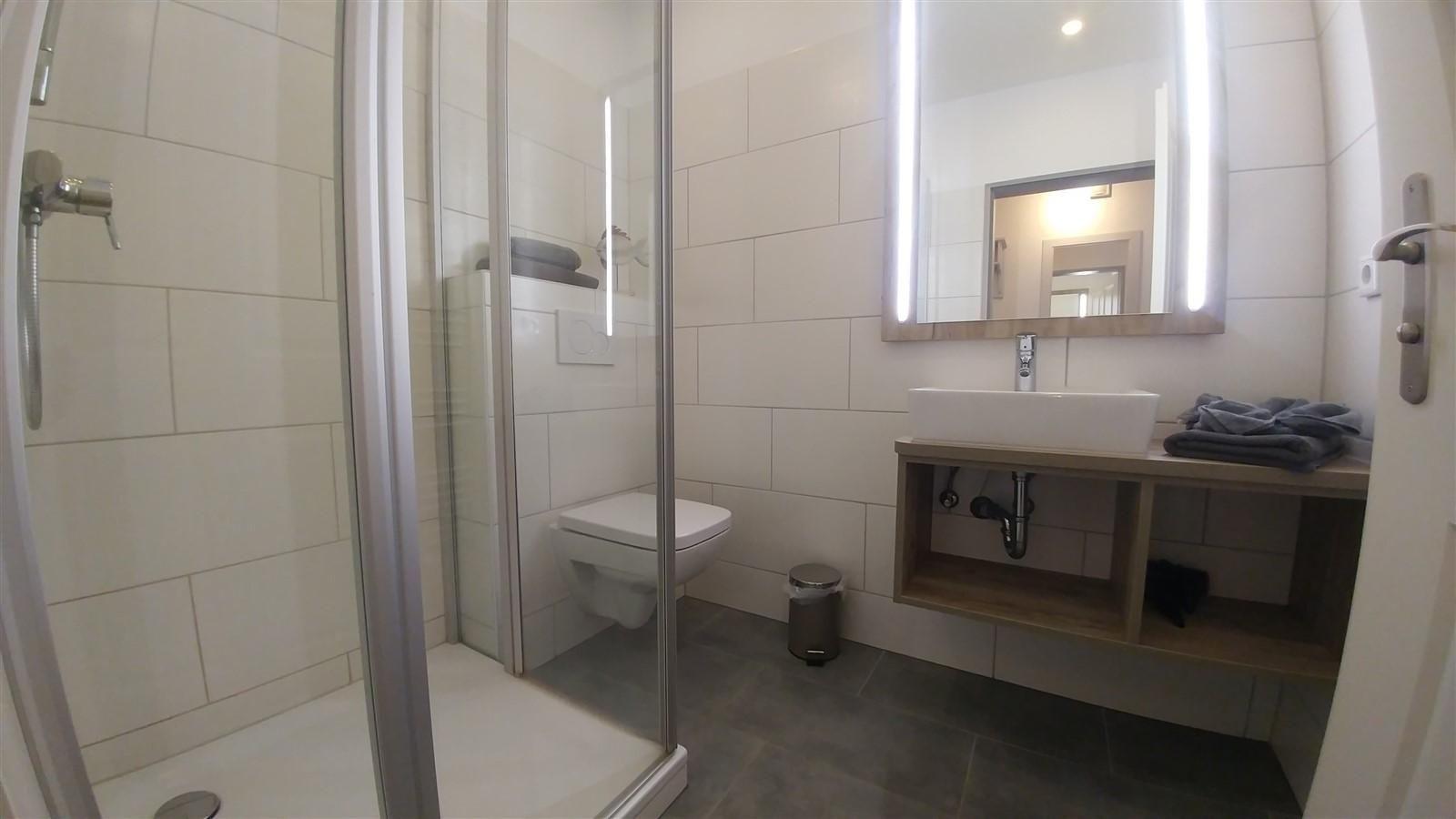 Badezimmer mit Dusche, Toilette und Waschbecken mit beleuchtetem Spiegel.