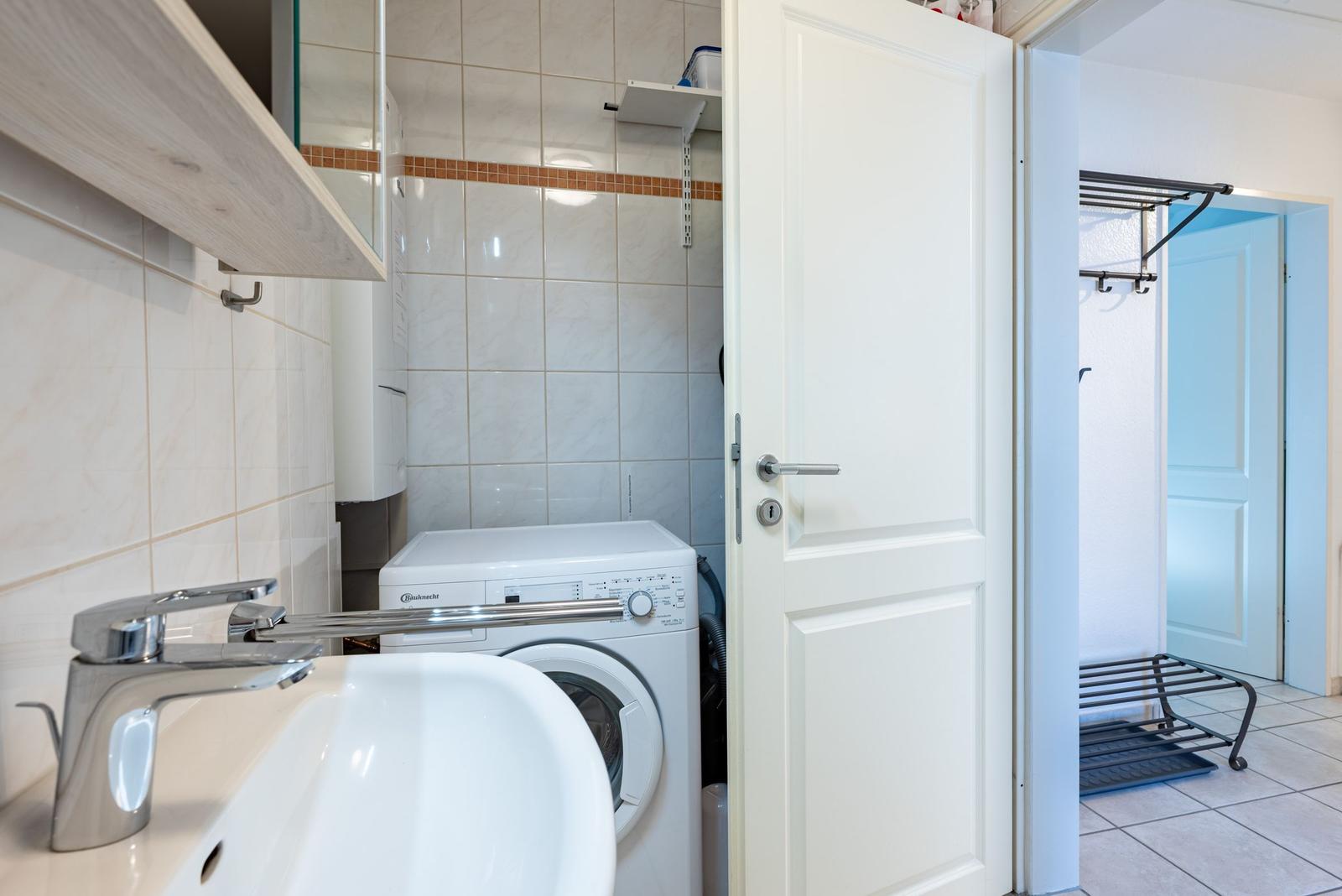 Waschmaschine und Waschbecken in einem Raum mit Fliesenwand und Tür.