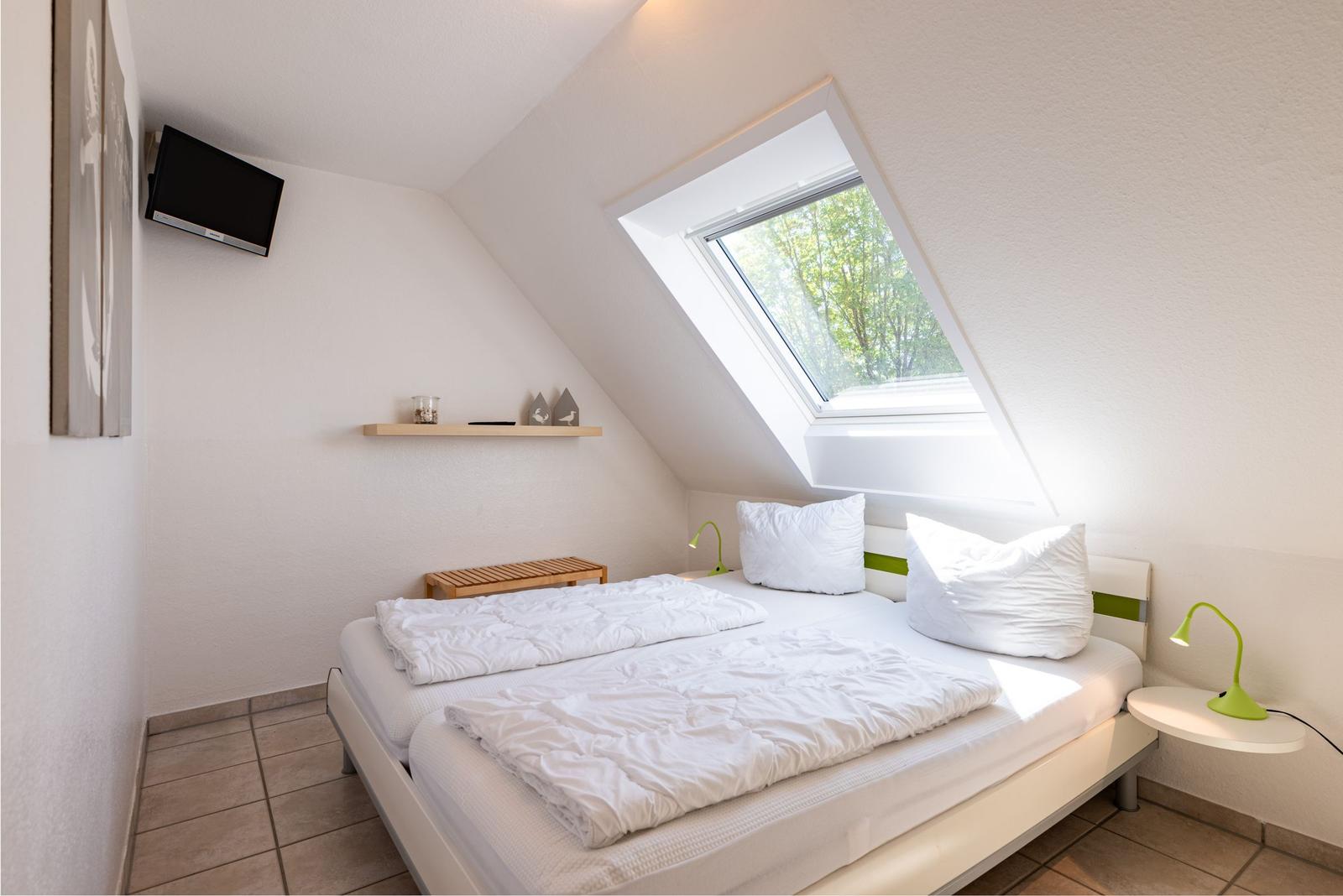 Schlafzimmer mit Dachfenster, Bett, Nachttisch und Fernseher an der Wand.