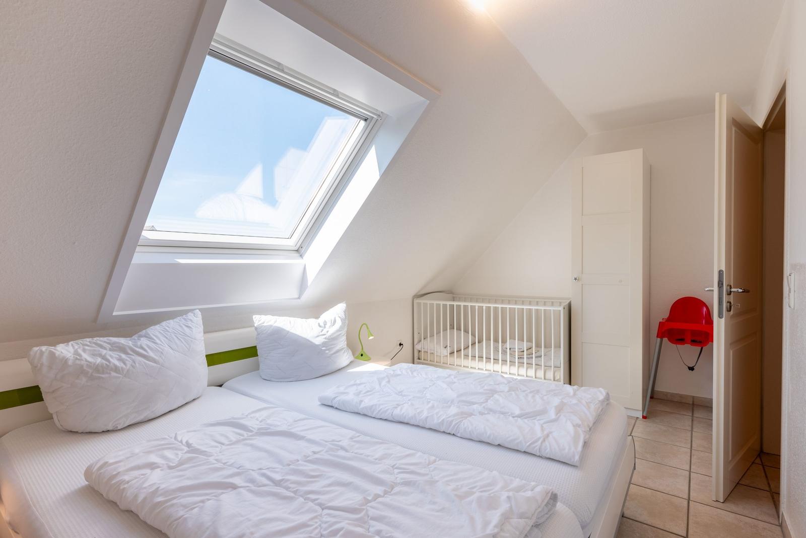 Schlafzimmer mit Dachfenster, Bett und Kinderbett. Roter Stuhl im Flur.