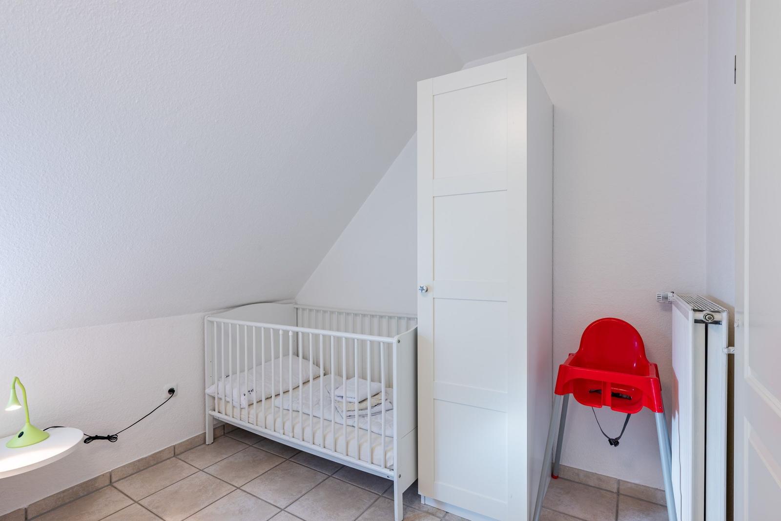 Kinderzimmer mit Babybett, Kleiderschrank und roter Hochstuhl.