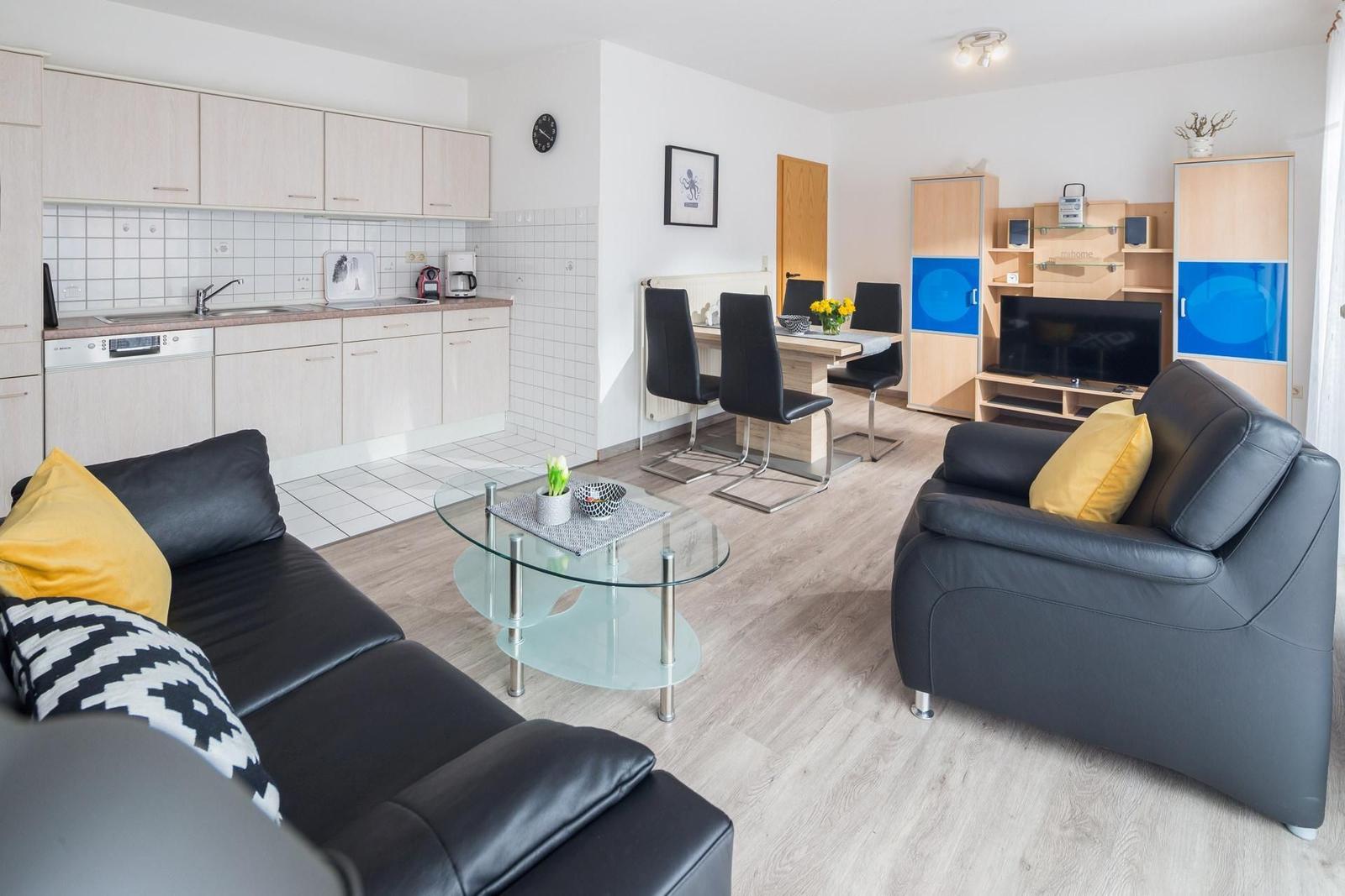 Wohn- und Essbereich mit Küche, Sofa, Sessel und Fernseher.